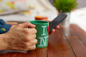 Mujer sujeta una taza de café mientras observa su teléfono.