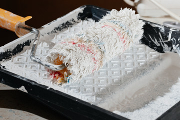 Paint roller with a brush paints the shelves and walls pours and flows with white paint