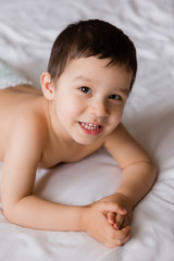 Cute toddler boy in diapers lies on bed with white sheet