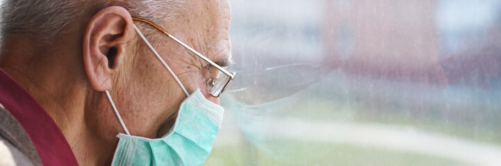 old man wearing face mask and glasses looking through window stay at home