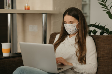 Remote work. A woman in a medical face mask working remotely on her laptop during the quarantine to avoid the spread coronavirus. A girl in a face mask at home during the pandemic of COVID-19