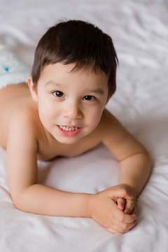 Cute toddler boy in diapers lies on bed with white sheet