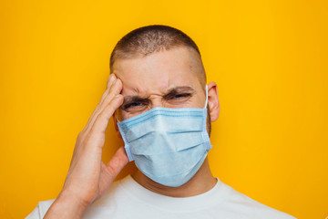 The guy holds on to his head, indicating that it hurts. Attractive man in a mask looks at the camera. Colds, flu, virus, tonsillitis, acute respiratory infections, quarantine, epidemic concept.