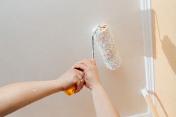 Paint roller with a brush paints the shelves and walls pours and flows with white paint