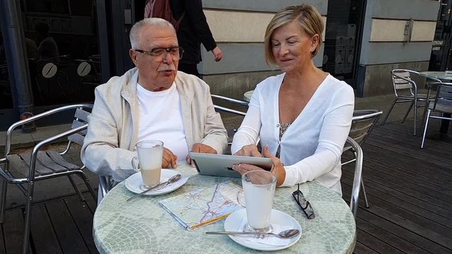 zoom in eldelry couple wearing white clothes and sitting in beautiful summer restaurant terrace in front of green bush