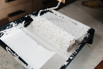 Paint roller with a brush paints the shelves and walls pours and flows with white paint