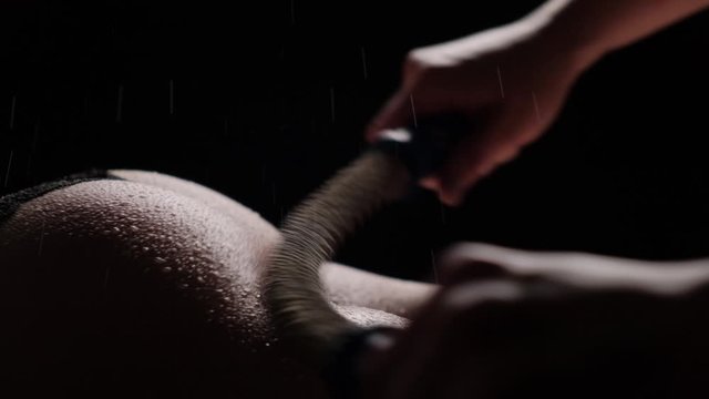 Close-up of a girl's skin massage using an Inari spring massager. Wet skin and splashes of water. Beautiful female ass.