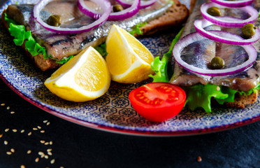 Appetizing smorrebrod with Norwegian herring, lettuce, blue onion, lemon and tomato lies on a...