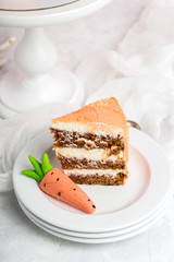 Piece of festive cream cake with mastic carrot, stack of white saucers, white background, vertical format.
