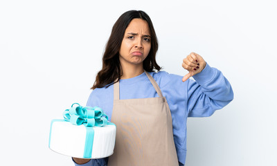 Pastry chef holding a big cake over isolated white background showing thumb down with two hands