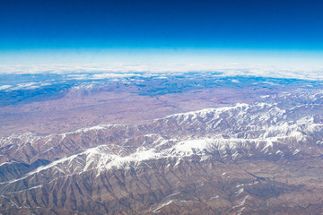 Mountains with snowy peaks from the window of an airplane on a sunny day.