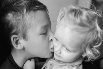 Black and white close-up portrait of siblings. Loving and careful brother kissing little sister on the cheek