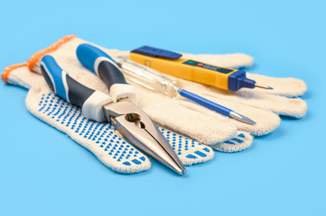 .Electrician's tool. Pliers, gloves, tester on a blue background.