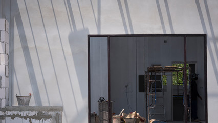 Sunlight and shadow on surface of concrete wall with construction material and equipment in door frame inside of house construction site