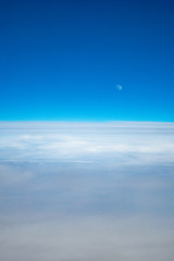 The moon above the clouds from an airplane on a sunny day.