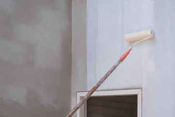 Long handle roller brush applying primer white paint with door frame on cement wall inside of house...