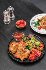 grilled meat with mushrooms red pepper onion grilled eggplant with red sauce on a black plate on a dark wooden background