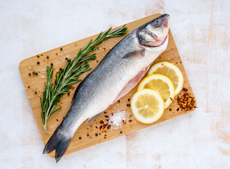 Fresh uncooked seabass with lemon, rosemary and spice on wooden cutting board over white backdground. Top view Healthy and diet food concept. Copy space