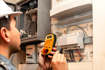 Service man with multimeter in hands adjusts electric control panel