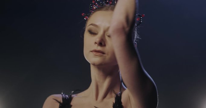 Close up of Caucasian young beautiful professional ballerina in jewellery crown on head dancing and doing pas in darkness. Portrait of ballet dancer moving and rehearsing.