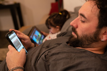 father and daughter with pacifiers on the sofa while using a tablet and a phone during quarantine