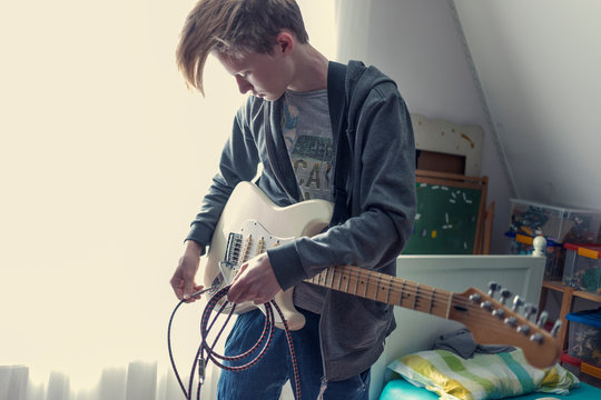Teenage boy is dreaming about a new song. In his room he is playing around on the  guitar.