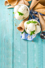 Homemade white vanilla ice cream balls with mint leaves in small portioned white bowl. With ice cream waffle cone and spoon,  on rustic turquoise wooden table, copy space