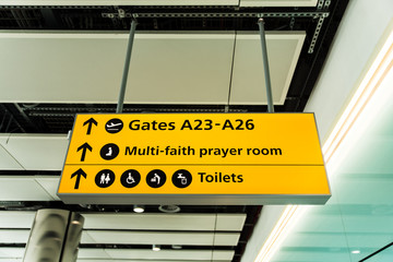 Yellow illuminated airport sign pointing the direction to gates, toilets and multi-faith prayer room