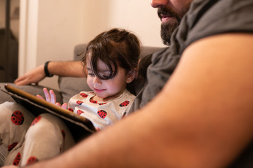 father and daughter on the sofa while learning on a tablet during quarantine