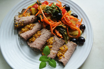 On a white plate, slices of chopped beef roast beef and salad with sauce