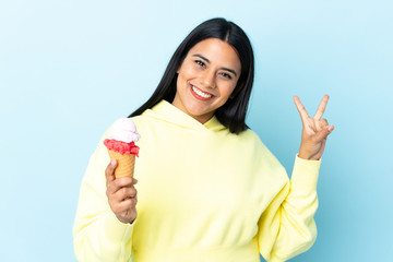 Young Colombian woman with a cornet ice cream isolated on blue background smiling and showing victory sign