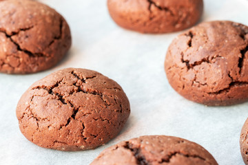 Fototapeta na wymiar Baked cracked round chocolate cookies on a baking sheet with parchment paper just taken out of the oven. Tea snack. Selective focus. Closeup view