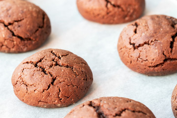 Baked cracked round chocolate cookies on a baking sheet with parchment paper just taken out of the oven. Tea snack. Selective focus. Closeup view