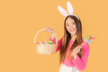 Beautiful asian young woman wear bunny ears standing smiling and holding basket with easter eggs