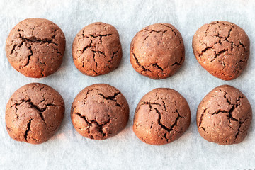 Baked cracked round chocolate cookies on a baking sheet with parchment paper just taken out of the oven. Tea or coffee snack. Closeup top view