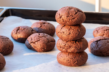 Baked cracked round chocolate cookies piled up on top of each other on a baking sheet with parchment paper just taken out of the oven. Tea or coffee snack. Selective focus. Closeup view