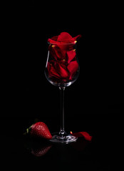 glass with rose petals and strawberries on a black background