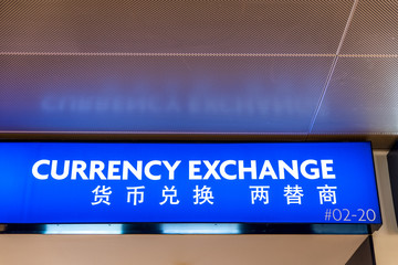 Close up of blue light currency exchange sign at international airport. Translation in English and Chinese