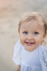 Girl blue-eyed blonde in a white dress runs on the waves of the sea and laughs at sunset. high key, upper half.