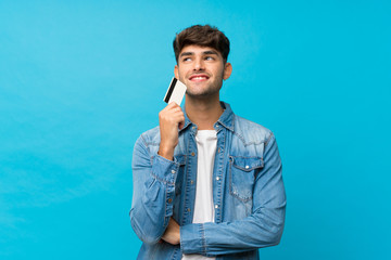 Young handsome man over isolated blue background holding a credit card