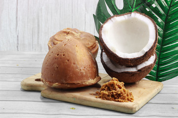 Jaggery or sugar from palm or coconut with half of coconut and leaf on wooden background