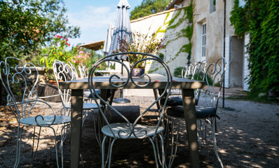Flowery farm backyard with wooden table and chairs at sunny summer day. Open summer patio with white wrought iron furniture.