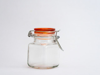 A small empty glass jar with orange lid shot agains white background and copy space.