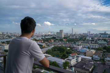 Fototapeta na wymiar Asian young man stay at home and watching cityscape from his balcony during covid-19 situation