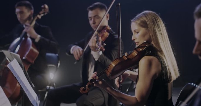 Profession symphony orchestra playing on violins and cello at concert. Male and female musicians play on stage in theater. Classical art concept.