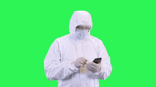 Masked man in protective suit surfing the phone while standing against green background