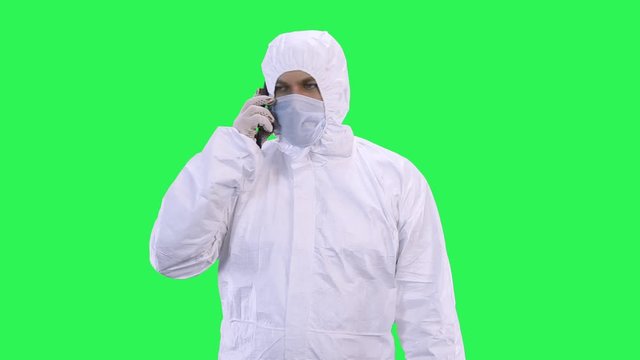 A man in a protective suit and a protective mask and glasses is talking on the phone.