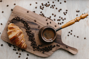 Turkish coffee pot, croissant and coffee beans on wooden board