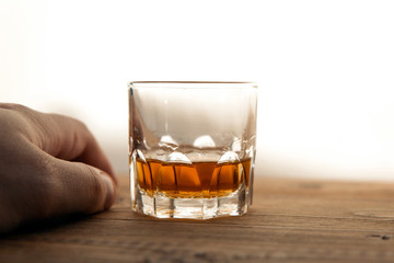 Glass with whiskey, next to a male hand
