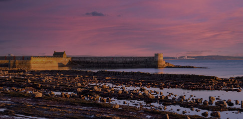 Obraz premium Sunset Reflecting off the harbour Walls of Old Saltcoats Pier on the Clyde in Scotland.